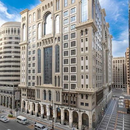 Al Aqeeq Madinah Hotel Medina Exterior foto The photo depicts a large, modern building with a distinctive architectural style. The structure shows a blend of classic and contemporary design elements, featuring ornate details, large glass windows, and a prominent central facade. Surrounding the