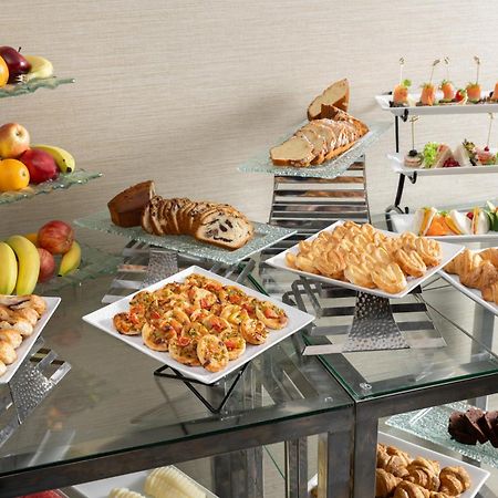 Al Aqeeq Madinah Hotel Medina Exterior foto The photo showcases a buffet-style spread featuring a variety of food items. There are several platters with appetizers, including seafood dishes, pastries, and other savory items. In addition, there is a selection of fresh fruit displayed on a glass