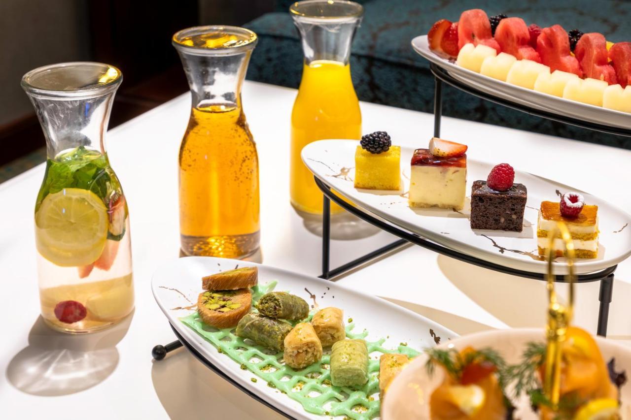 Al Aqeeq Madinah Hotel Medina Exterior foto The photo showcases an elegant display of refreshments and desserts. There are several glass pitchers filled with bright, colorful beverages, likely juices or infused water, one featuring lemon and mint. A two-tier serving stand holds an assortment o