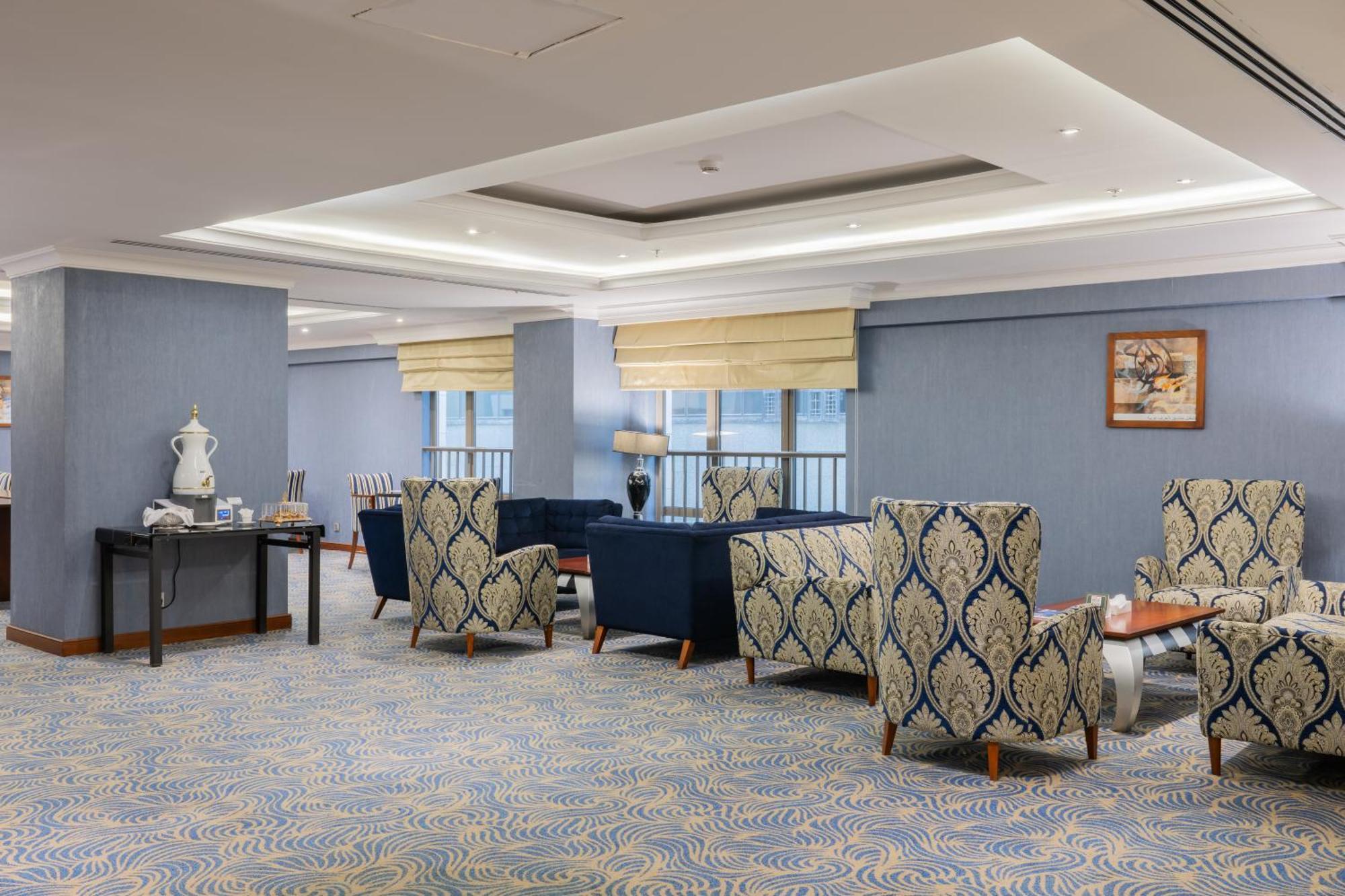 Al Aqeeq Madinah Hotel Medina Exterior foto The photo shows a stylish indoor lounge or sitting area. It features several upholstered armchairs arranged around a central space. The chairs have a blue and cream patterned upholstery, creating a sophisticated ambiance. There is a table alongside s