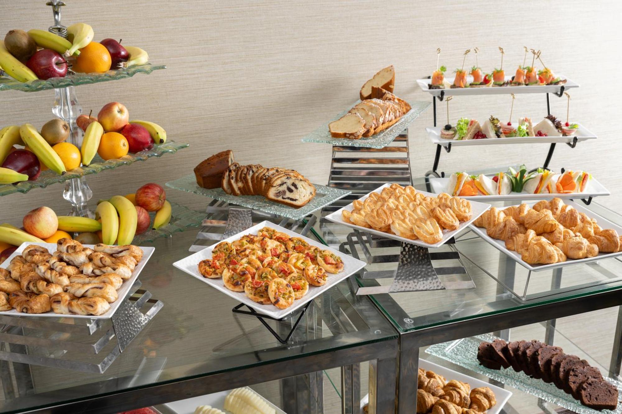 Al Aqeeq Madinah Hotel Medina Exterior foto The photo showcases a buffet-style spread featuring a variety of food items. There are several platters with appetizers, including seafood dishes, pastries, and other savory items. In addition, there is a selection of fresh fruit displayed on a glass