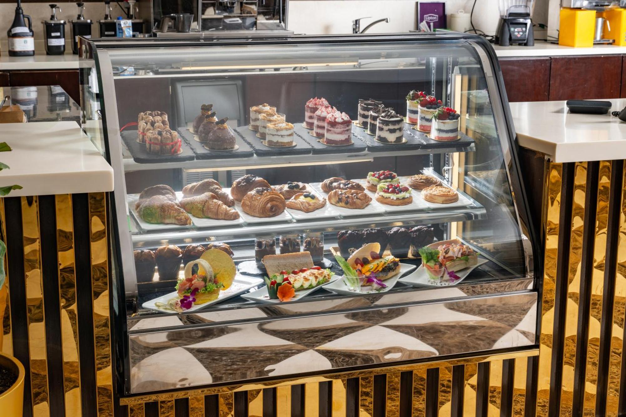 Al Aqeeq Madinah Hotel Medina Exterior foto The photo shows a display case filled with an assortment of desserts. There are various types of pastries, including cakes, tarts, and croissants, arranged neatly on different shelves. The desserts are visually appealing, with colorful decorations, f
