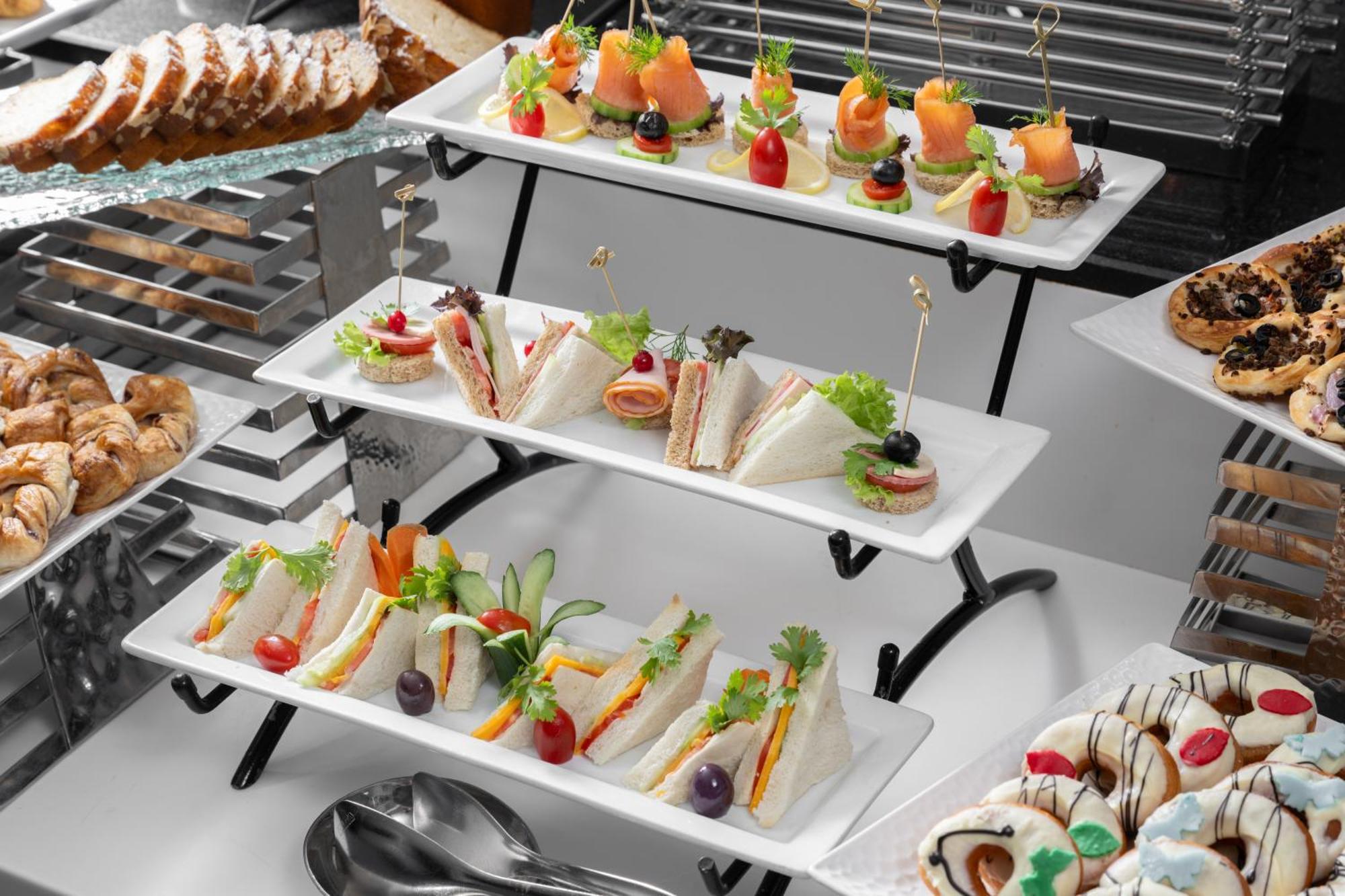 Al Aqeeq Madinah Hotel Medina Exterior foto The photo shows a tiered display of assorted appetizers and snacks arranged on white rectangular plates. 

1. **Top Tier**: Contains small bites featuring smoked salmon garnished with greenery, and some with colorful cherry tomatoes on toothpicks. 

