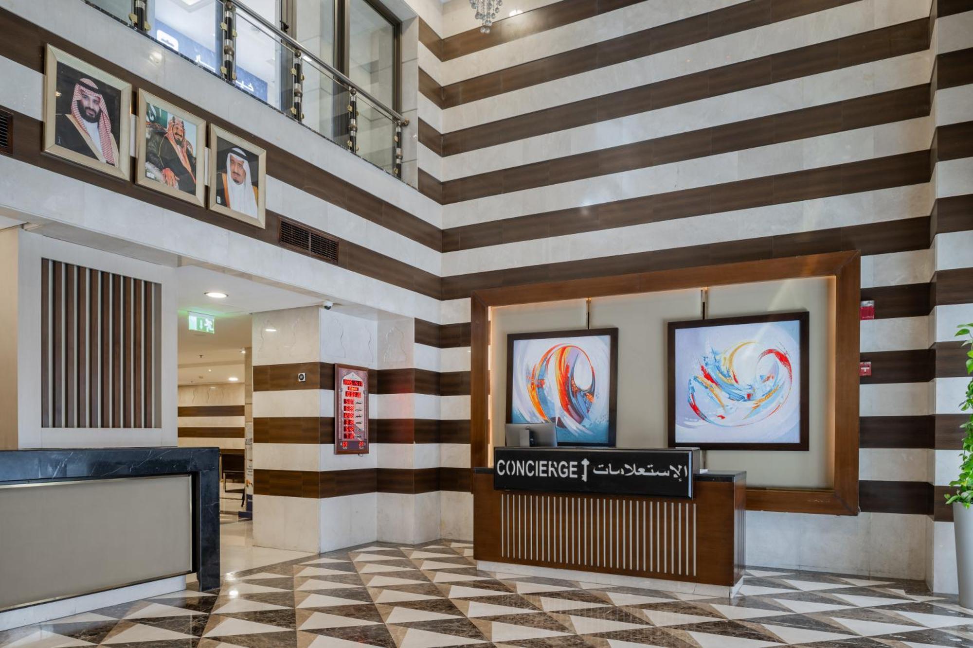 Al Aqeeq Madinah Hotel Medina Exterior foto The photo shows a modern hotel lobby area characterized by its stylish design. The walls feature a pattern of horizontal stripes in different shades, creating a sophisticated atmosphere. To the left, there is a reception area with a sleek desk labele
