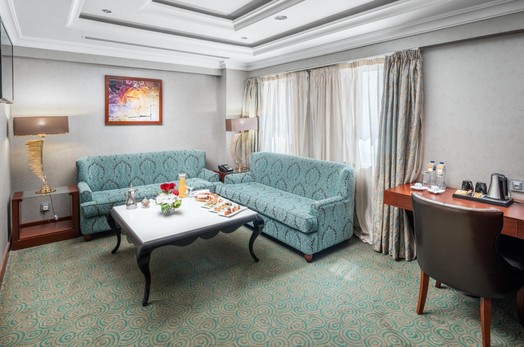 Al Aqeeq Madinah Hotel Medina Exterior foto The photo shows a cozy hotel room or lounge area. It features two light blue sofas arranged around a low coffee table. On the table, there are snacks or refreshments arranged aesthetically. The room has a neutral color palette with a textured carpet 