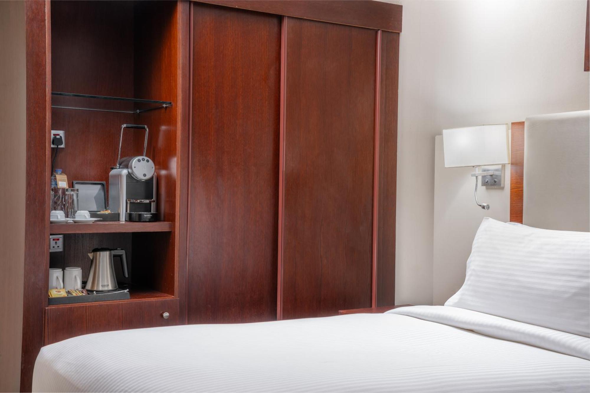 Al Aqeeq Madinah Hotel Medina Exterior foto The photo shows a hotel room with a minimalist design. On the left side, there's a wooden cabinet with sliding doors that houses a small coffee maker and additional amenities, such as cups and a kettle. The bed is neatly made with white bedding and i