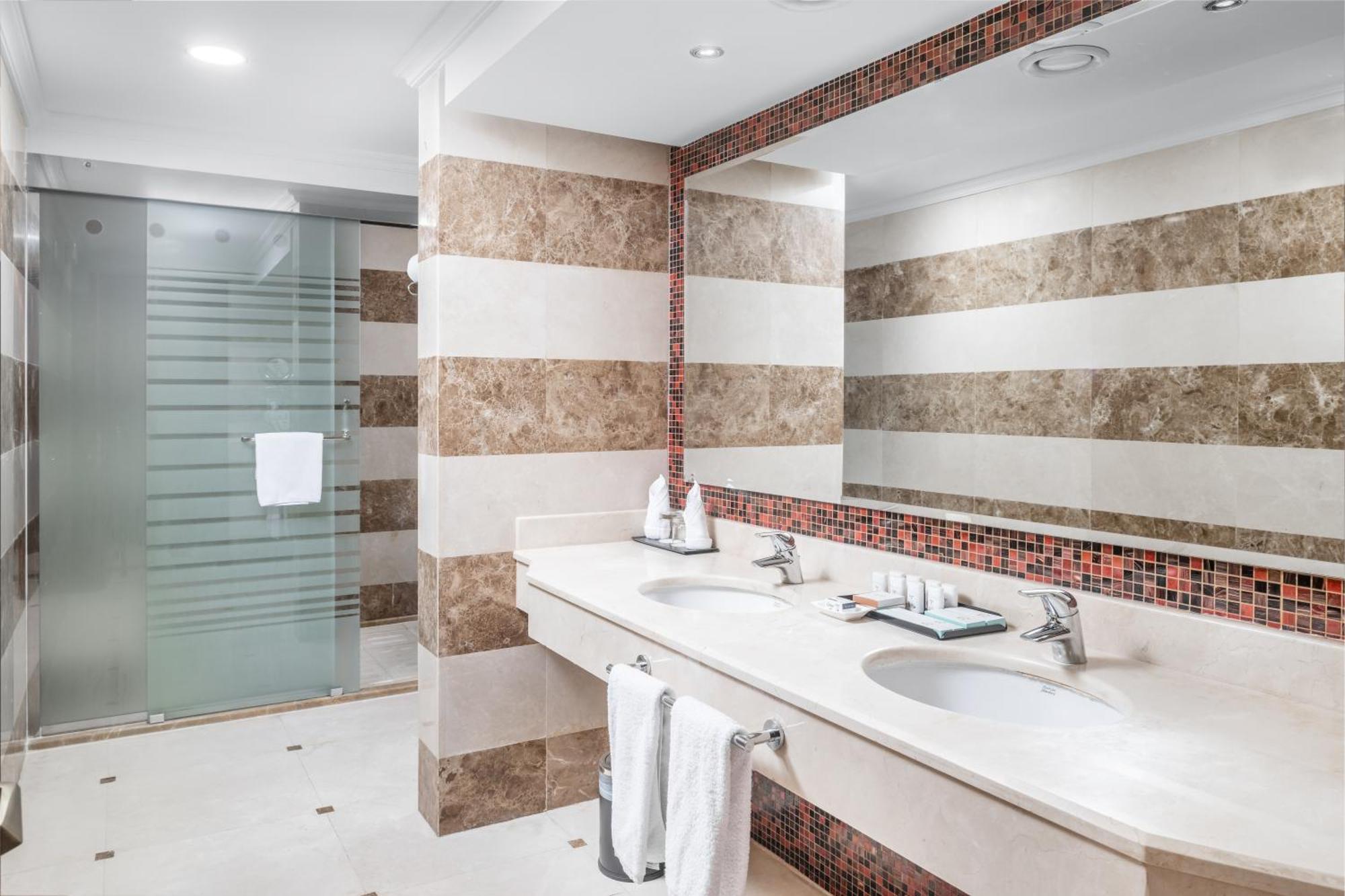 Al Aqeeq Madinah Hotel Medina Exterior foto The photo shows a modern bathroom with an elegant design. It features a large double sink with a smooth countertop, accompanied by faucets. The walls are adorned with alternating horizontal stripes of light and dark materials, creating a stylish look