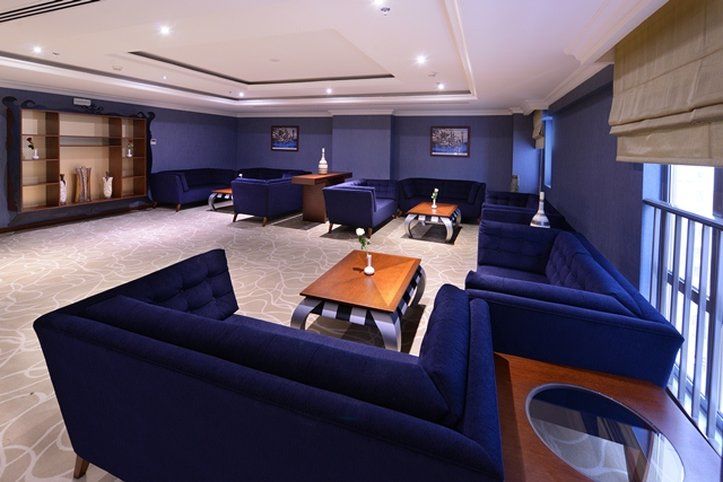 Al Aqeeq Madinah Hotel Medina Exterior foto The photo shows a modern lounge area featuring a sophisticated design. The room is painted in a deep blue color, creating a calm and elegant atmosphere. There are several dark blue sofas arranged around a central wooden coffee table. The table is dec