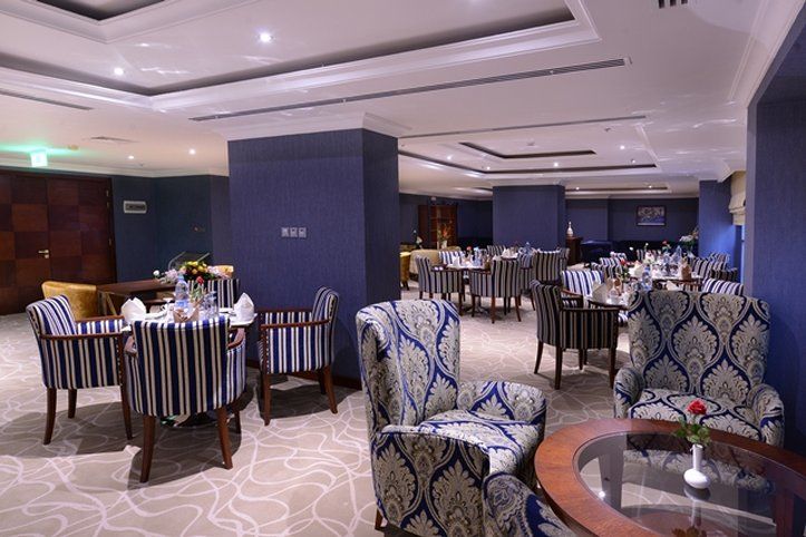 Al Aqeeq Madinah Hotel Medina Exterior foto The photo shows an elegant dining or lounge area. The space features plush seating with striped and patterned chairs, and tables set up for dining. The decor includes a rich color palette with blue walls and soft lighting creating a warm atmosphere. 