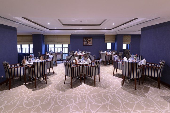 Al Aqeeq Madinah Hotel Medina Exterior foto The photo shows an elegant dining room equipped with several tables. Each table is set with white tableware and neatly arranged silverware, giving a formal dining appearance. The decor features striped chairs and a carpet with a subtle pattern. The w