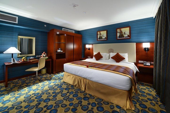 Al Aqeeq Madinah Hotel Medina Exterior foto The photo shows a hotel room designed with a modern and stylish aesthetic. It features a large bed with a cream-colored headboard and decorative pillows. The room is decorated with blue walls and patterned carpet, creating a cozy atmosphere. 

There 